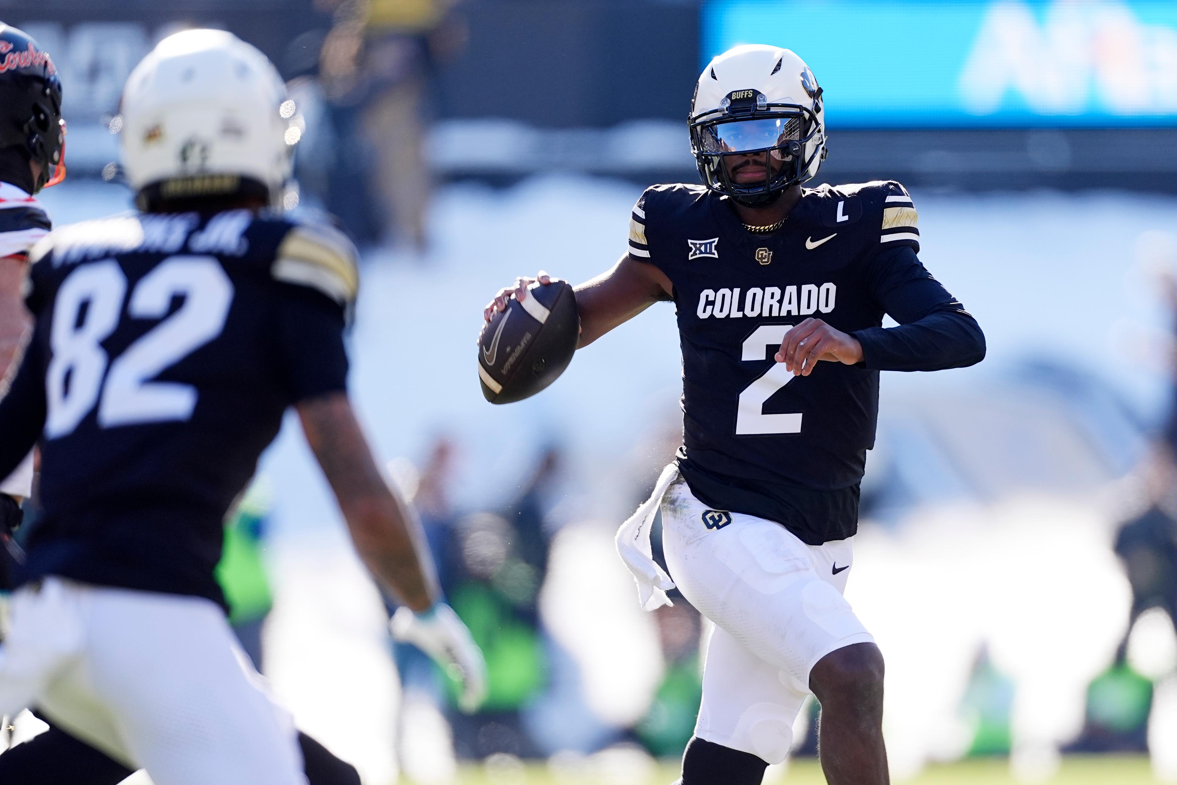 A man in a black jersey gets ready to throw a football with a receiver in the foreground.