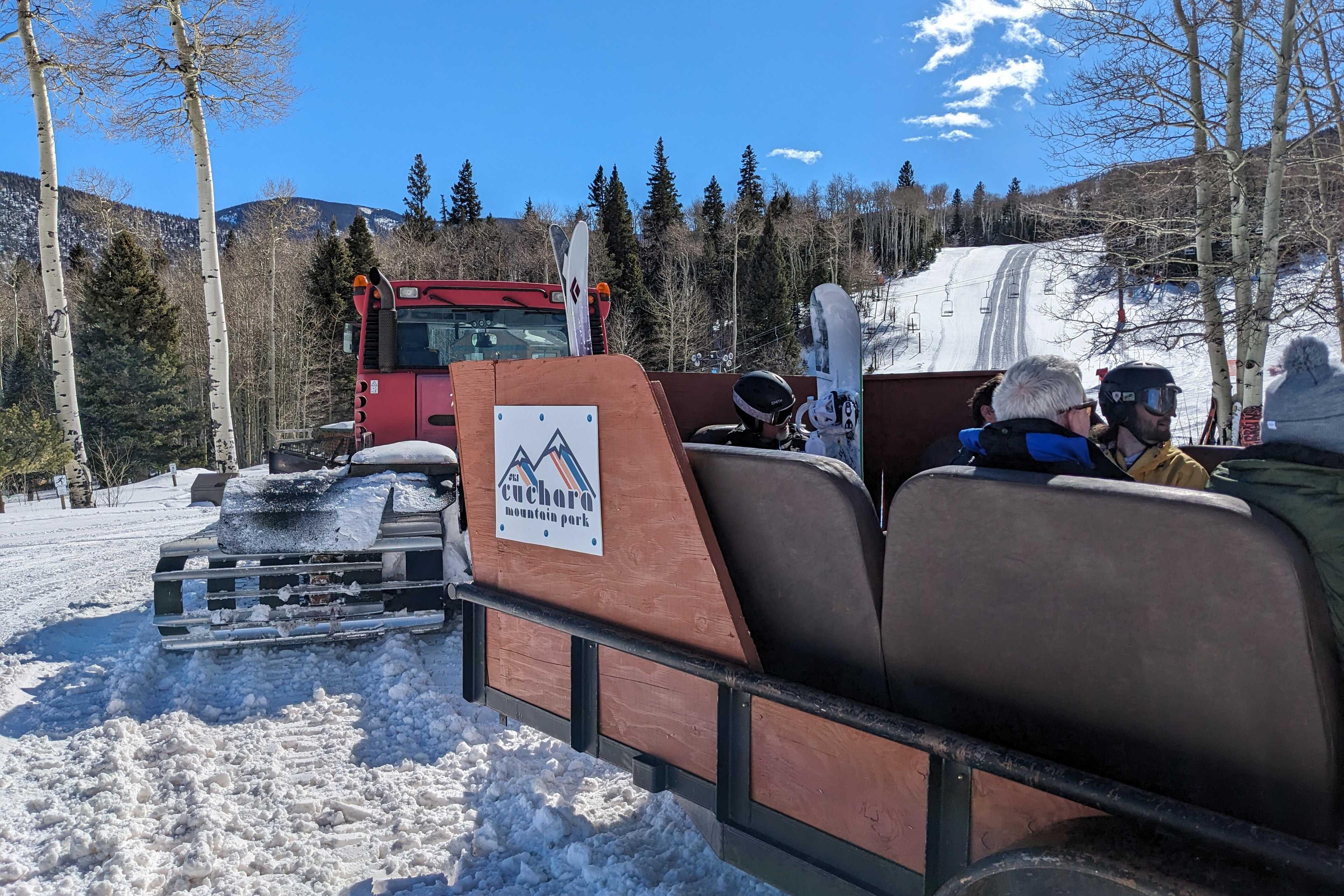 skiers and boarders sit in a trailer sled attached to a snow cat