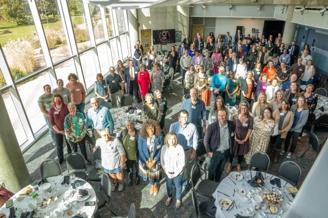 pic of a room full of people standing up posing in a room with windows