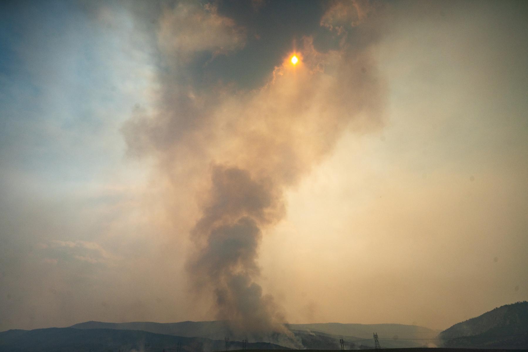 The image depicts a large, dark smoke cloud from the Lee fire billowing upwards. The smoke is rising above a field.