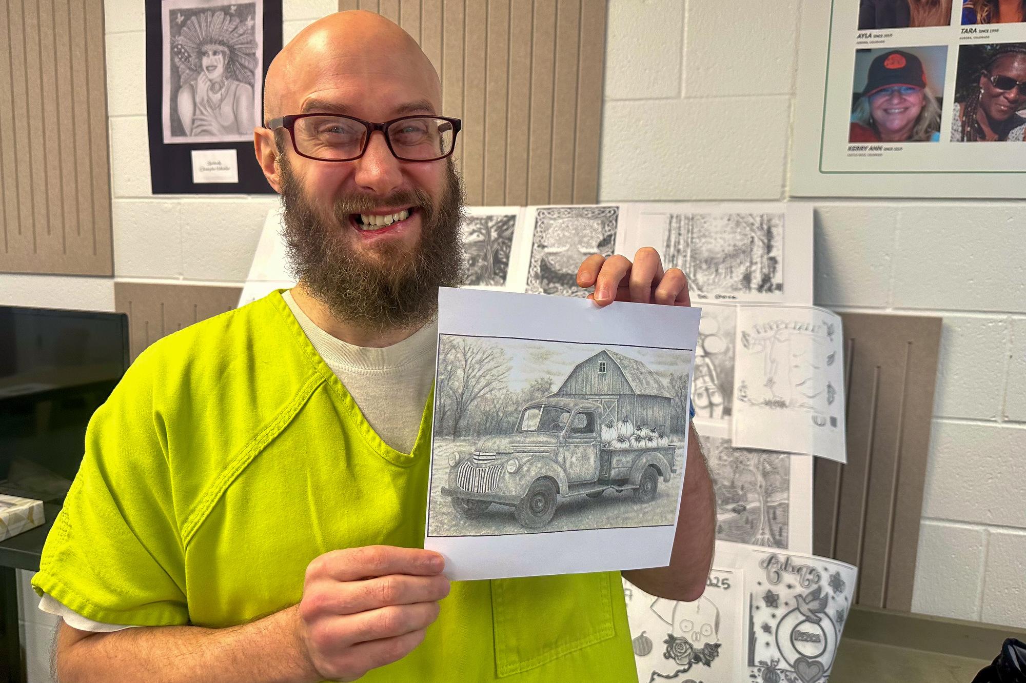 inmate holds up a photocopy of a drawing of an old truck with a bed filled with pumpkins in front of an old barn