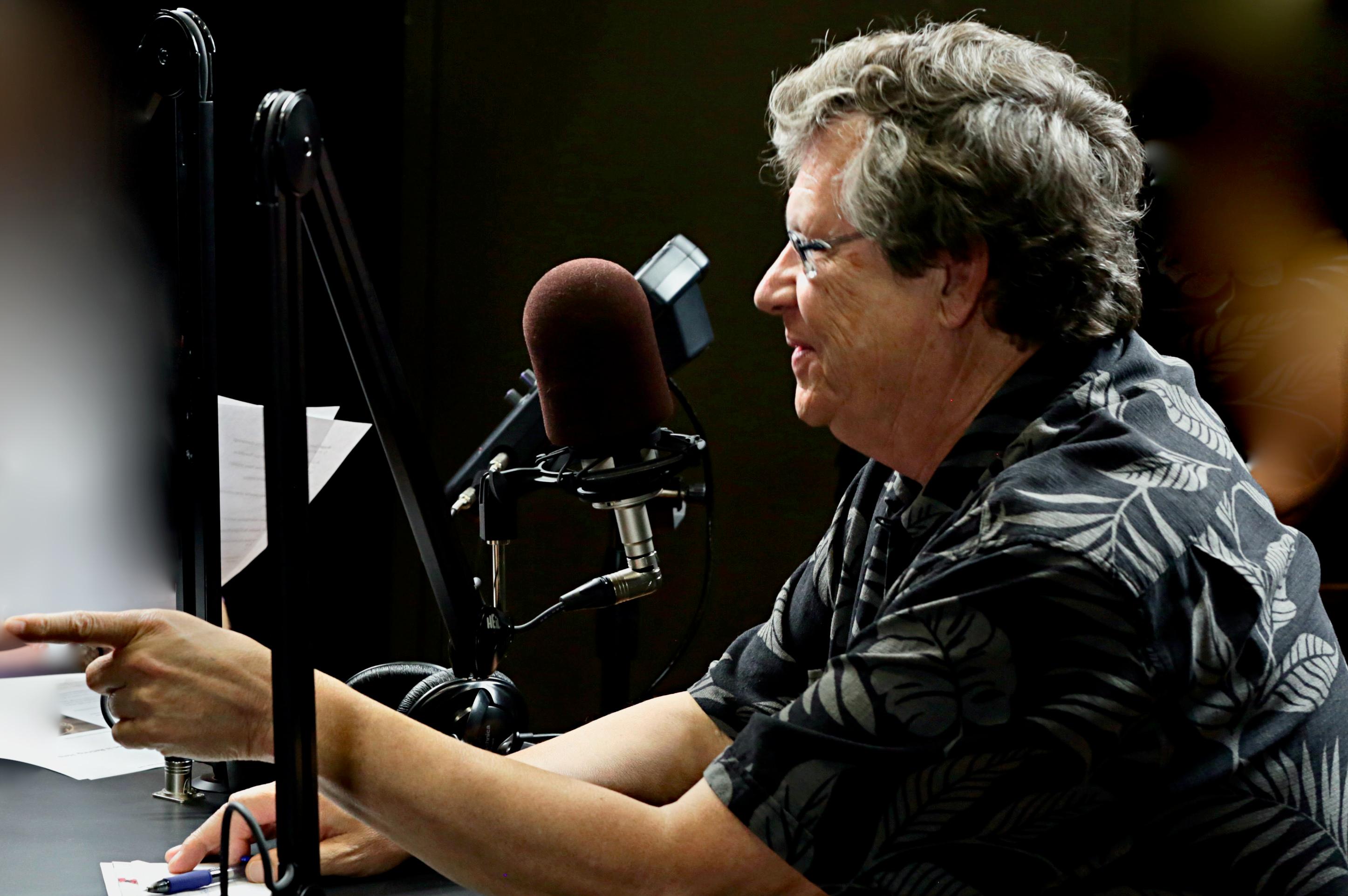 A man with glasses sitting in front of a radio microphone.