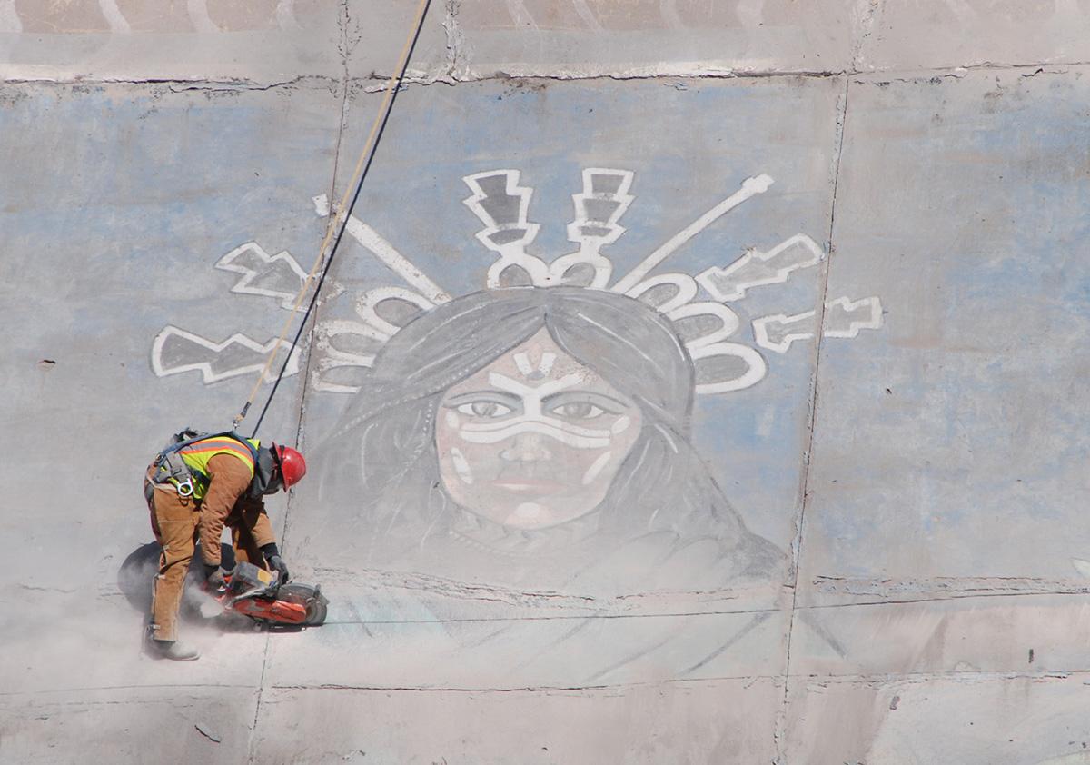 A worker is roped up for safety as he uses a special saw to cut through steel re-bar and concrete as the contractors work to save the Corn Maiden panel.