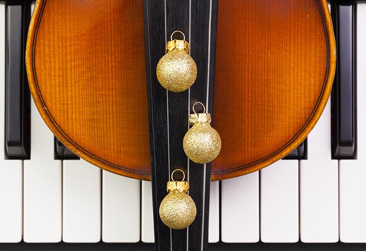 Close up shot of a piano keyboard with a violin and gold bulb ornaments on top