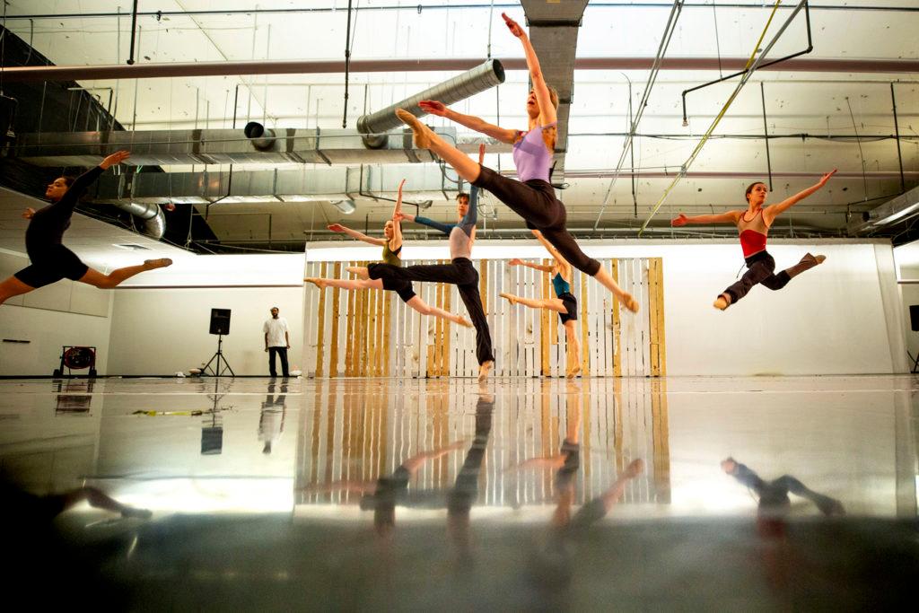 Ballet dancers leap through the performance space with their refelctions shining on the fllor.
