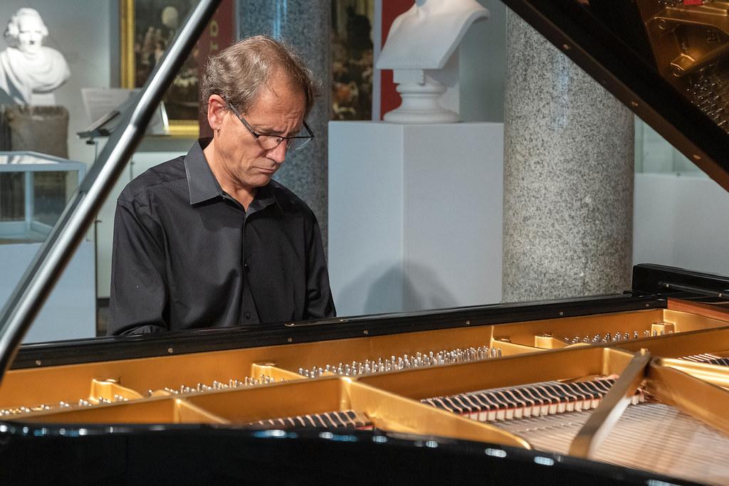 David Korevaar sits playing the piano with a classical bust in the background