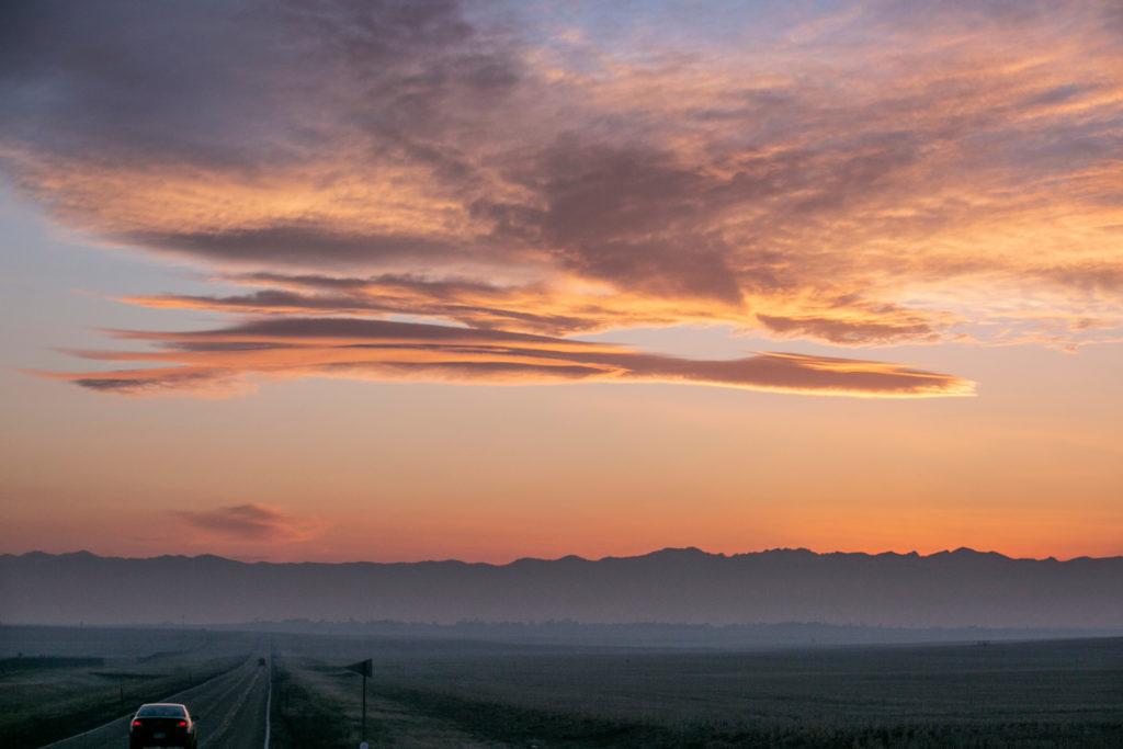 A car speeds westward in rural Adams County as the sun sets behind the Rocky Mountains