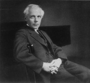 Black and white photograph of Bela Bartok seated with his hands clasped in front of him.
