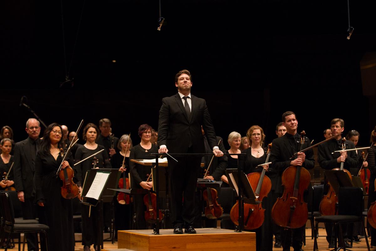 Brett Michell, conductor of the Colorado Symphony stands facing the audience with the symphony after a performance.