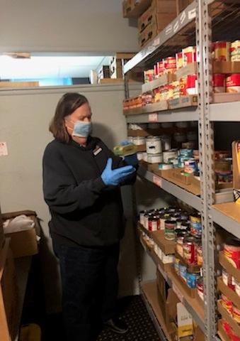 A picture of Laurie, in a face mask and gloves, choosing food from a large shelf.