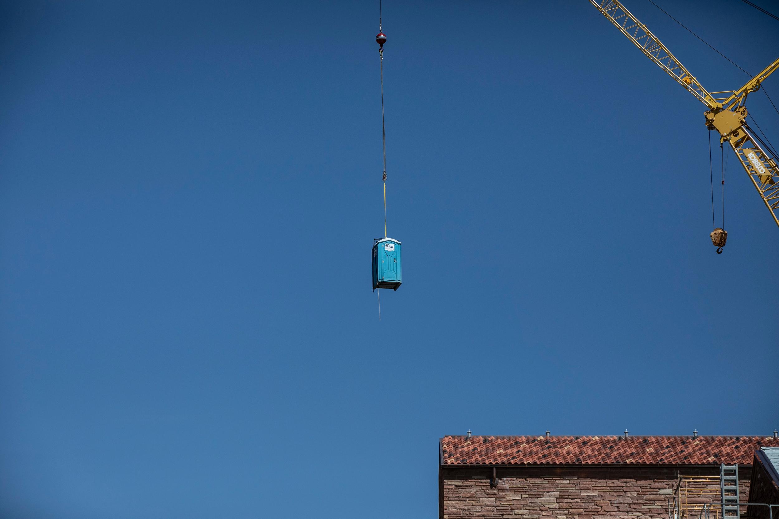 Crane lifts a portable toilet over a construction site at the University go Colorado at Boulder