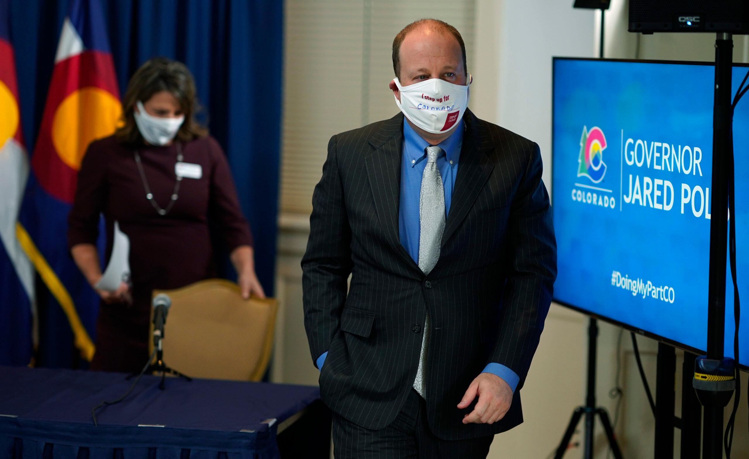 Jared Polis, front, and Jill Ryan, executive director of the Colorado Department of Public Health and Environment, leave after a news conference.