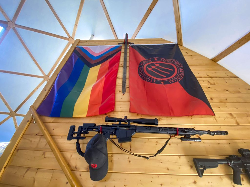 Various assault weapons and flags adorn the wall leading up to the ranch house’s second floor on April 27, 2021.