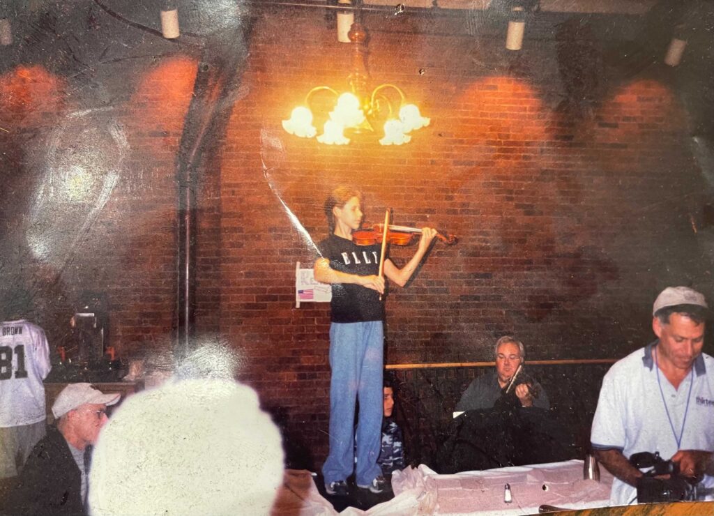 An 11-year-old Magee Capsouto stands on a table while playing the violin in a restaurant.