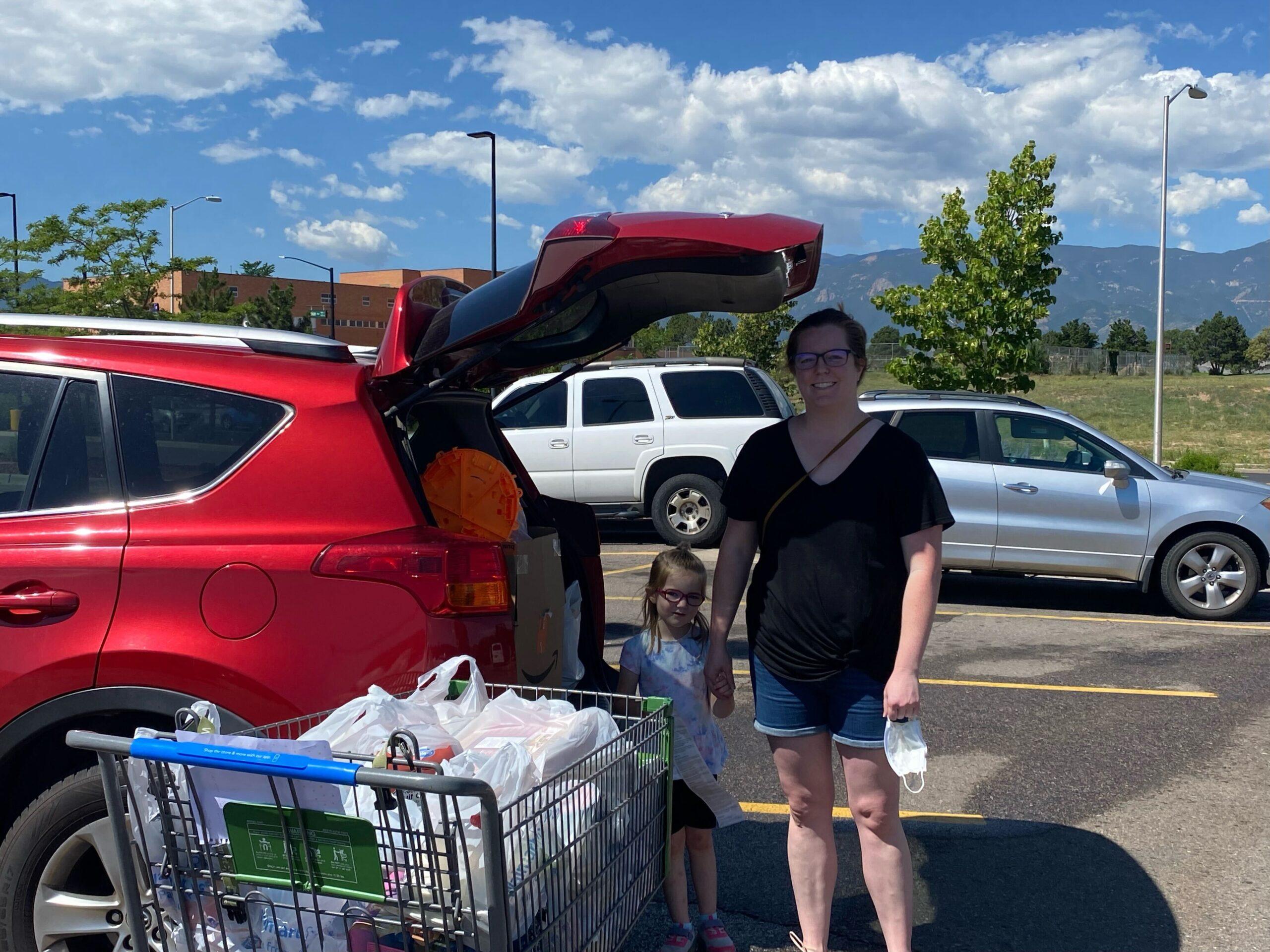A woman and her young daughter pose for a photo behind the open trunk of their vehicle with a filled shopping cart from Walmart.