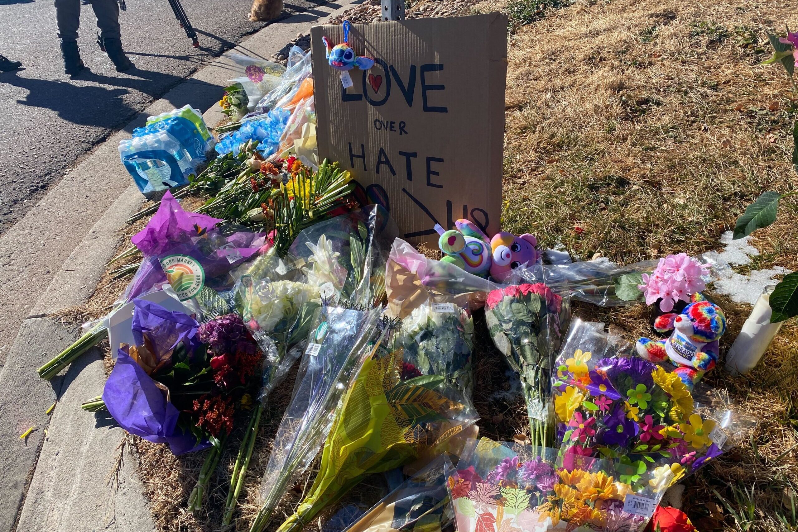 A cardboard sign with the words "Love over hate" sits next to flowers.