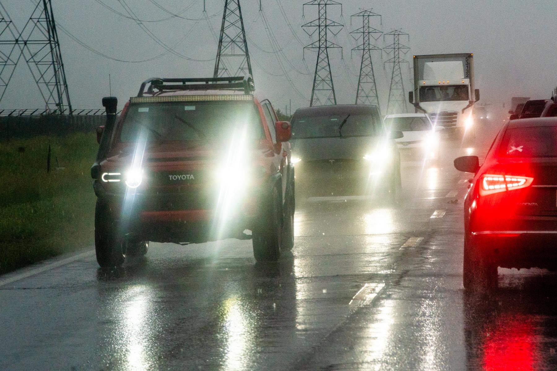 Cars on Gun Club Road turn on their headlights in the rain.