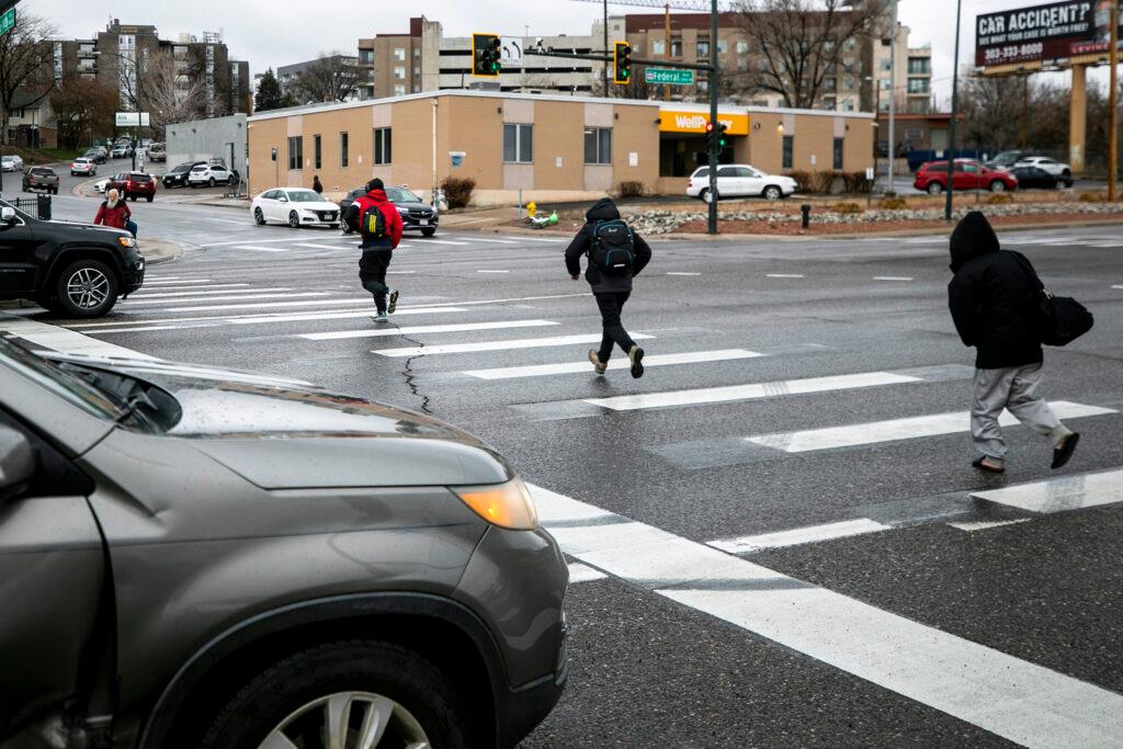 People run across Federal Boulevard to catch a bus. April 25, 2023.