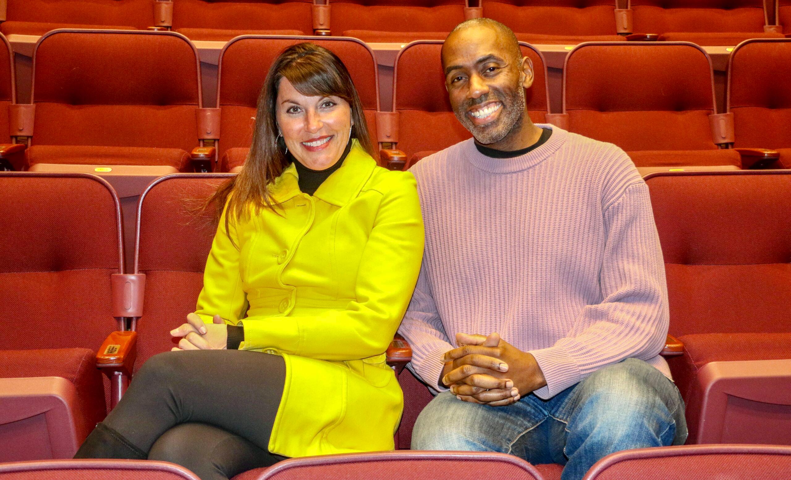 Ronni Stark and Kenny Moten, the new co-presidents of the Denver Actors Fund board, sit next to each other in red theater seats, smiling at the camera.
