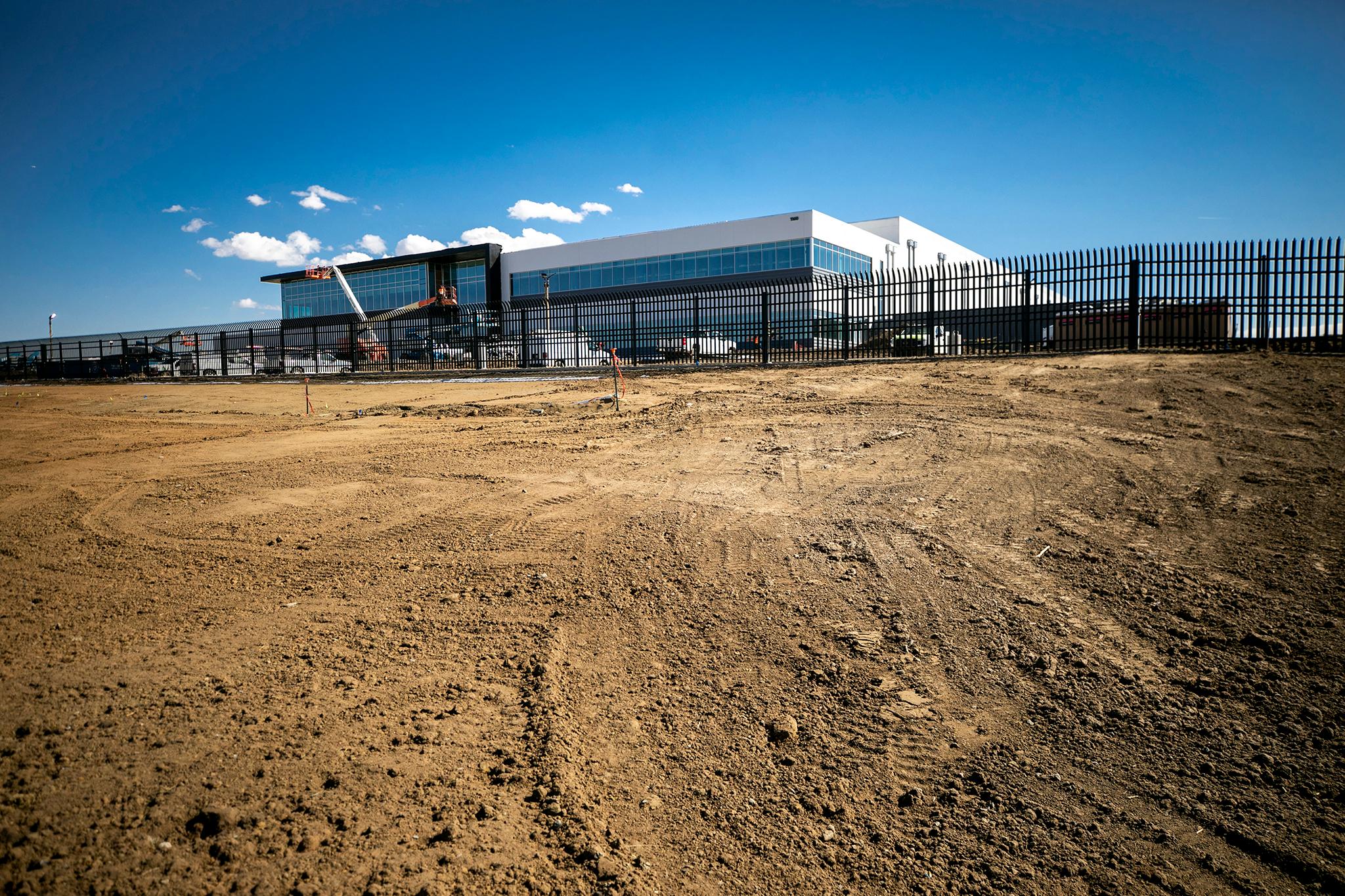 A large building sits at the top of a hill with an open field in front.
