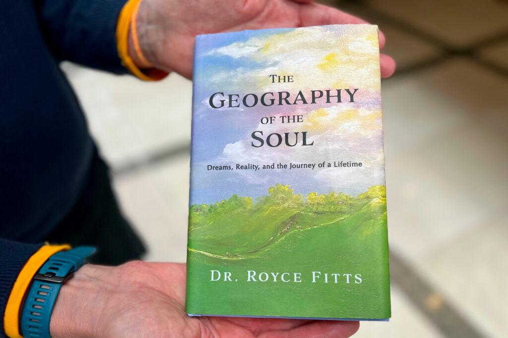 Dr. Royce Fitts holds a copy of his book, “The Geography of there Soul.”