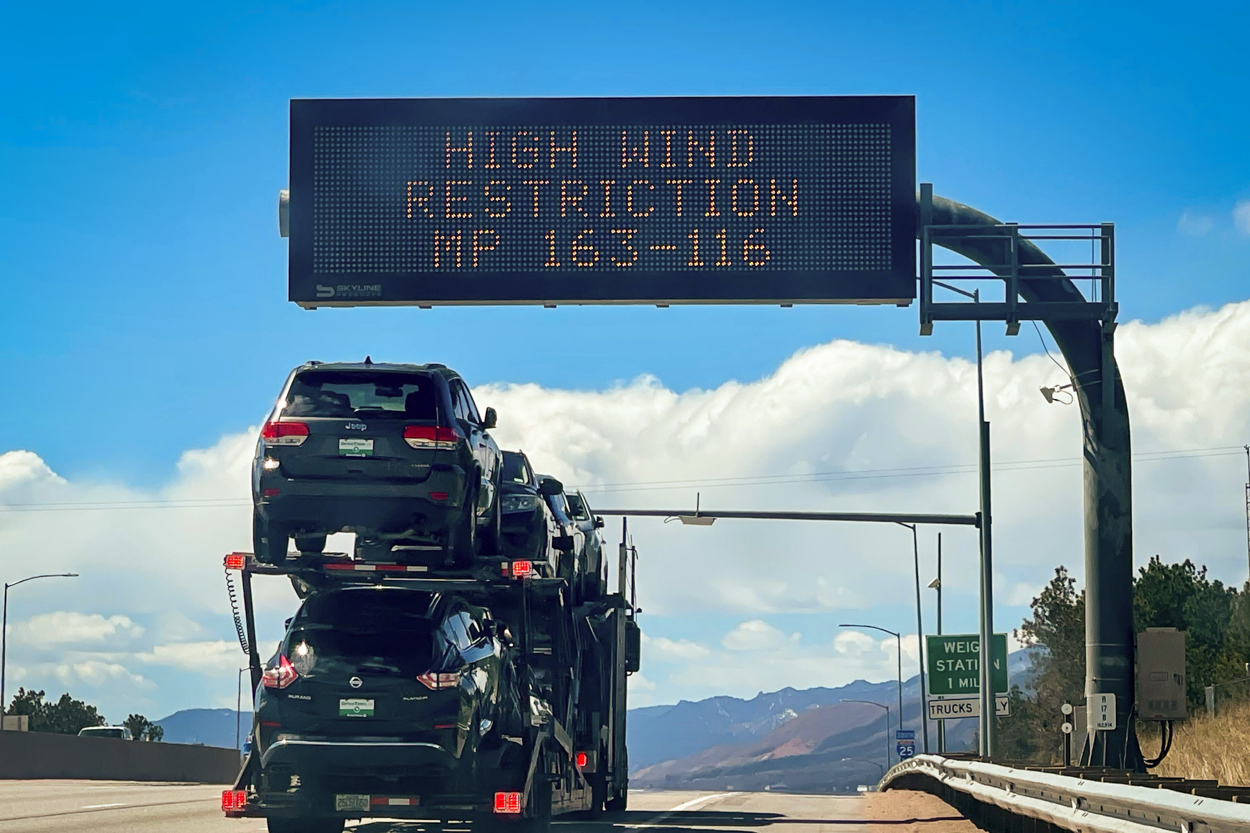Cars driving under a highway sign warning motorists about high winds.
