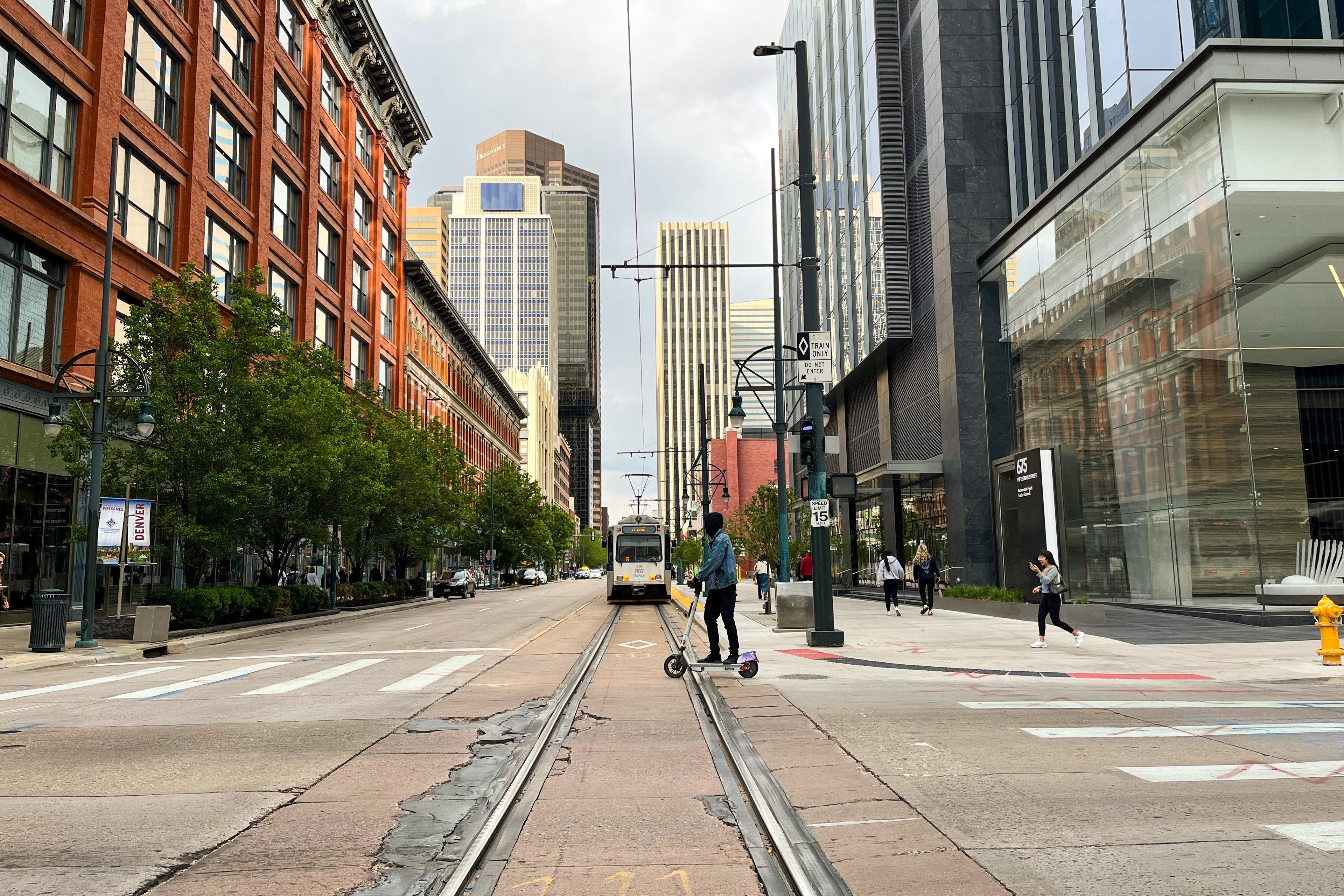 A picture of a scooter rider near a worn light rail section in downtown Denver.