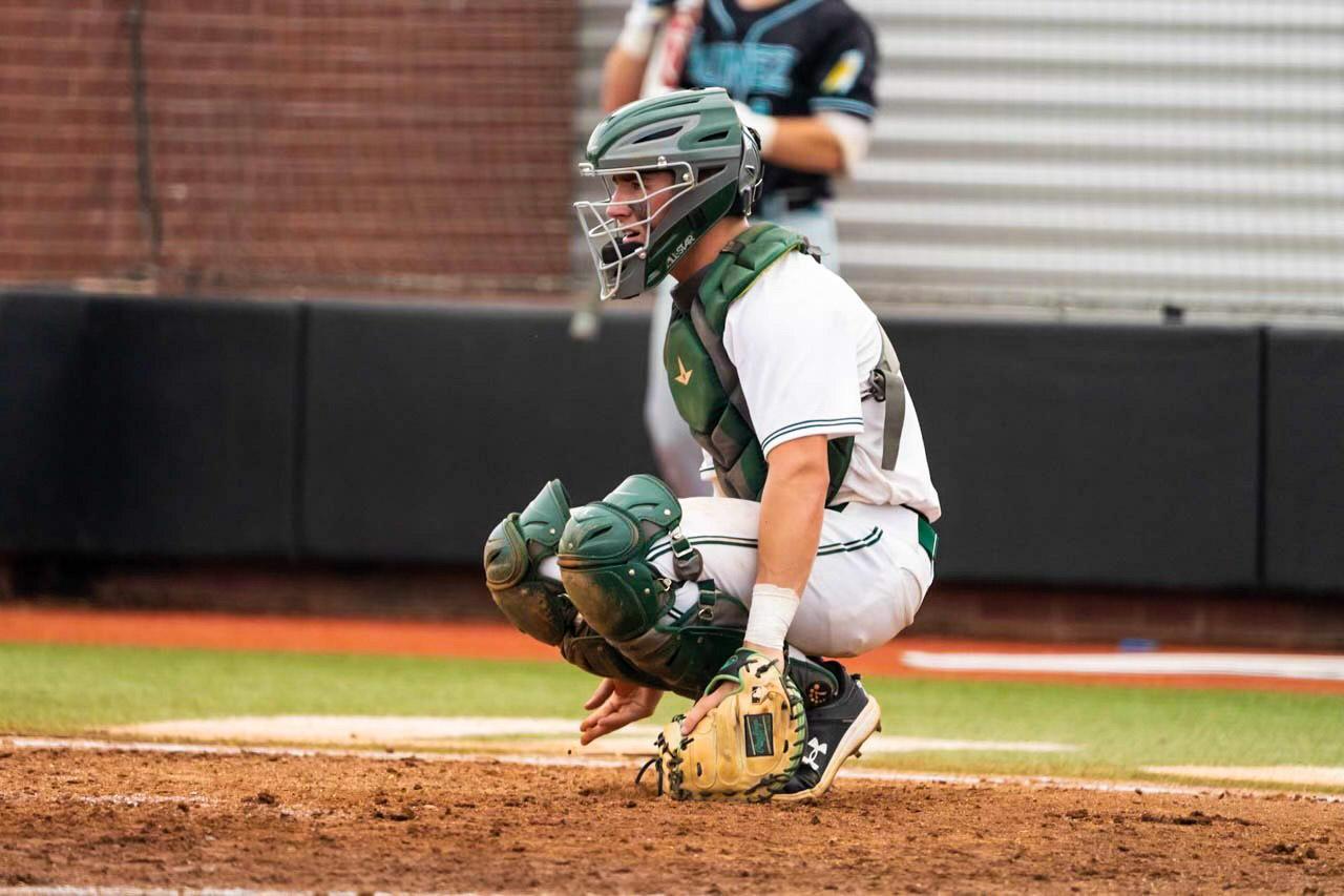 A baseball catcher crouched with his glove grazing the dirt