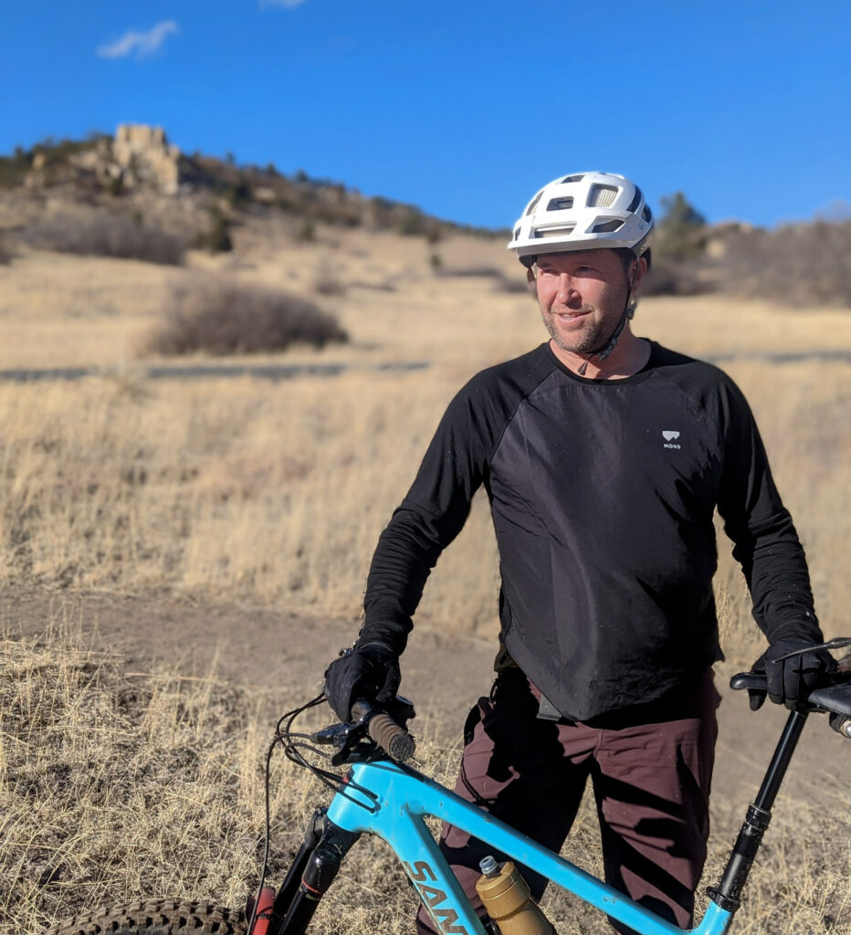 Keith Thompson of Keith Thompson of the Colorado Springs Mountain Bike Association (COSMBA) standing with his bike on a dirt trail.