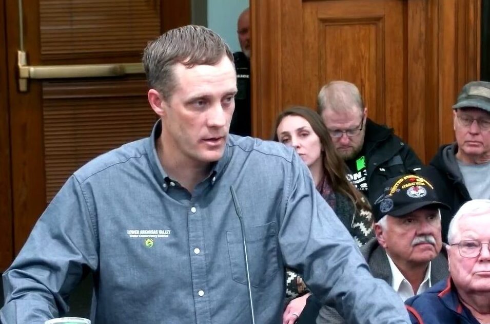 A man speaks into a microphone, people are seated behind him