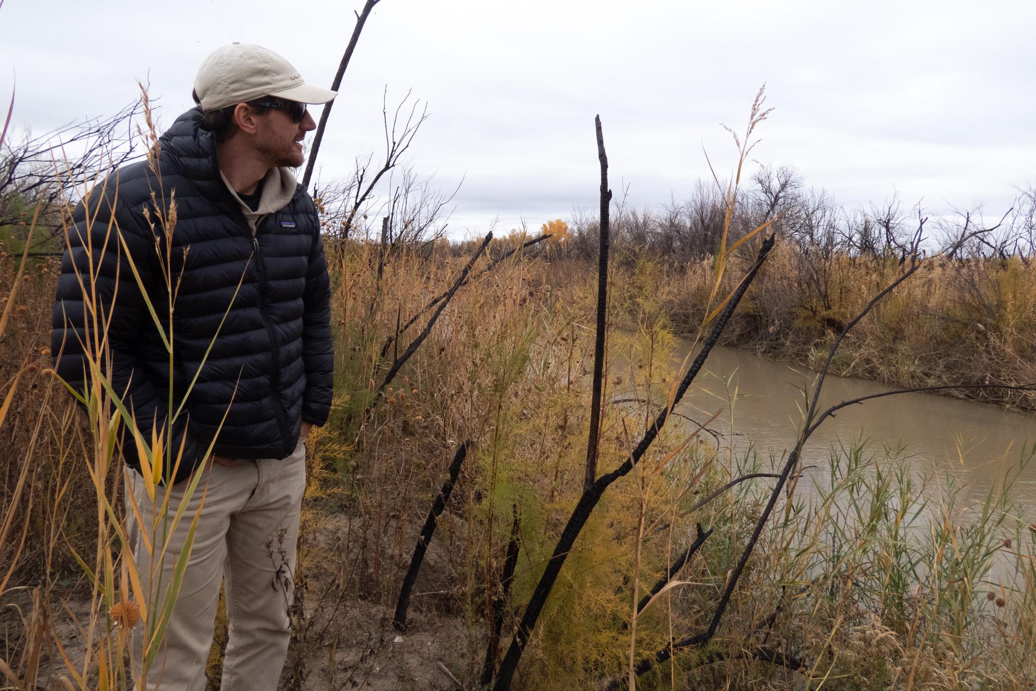 Man in warm clothes stands in brush near river