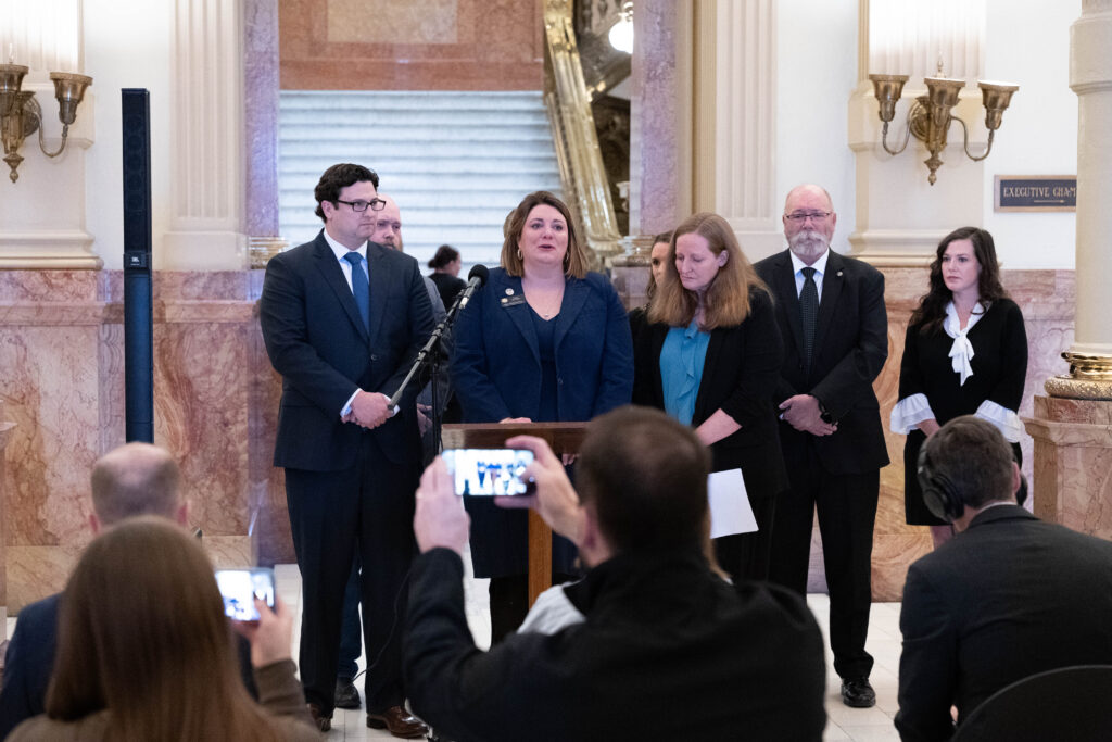 State Rep. Jenny Willford stands at a lecturn, flanked by her lawyers at a capitol press conference to discuss her lawsuit against Lyft.