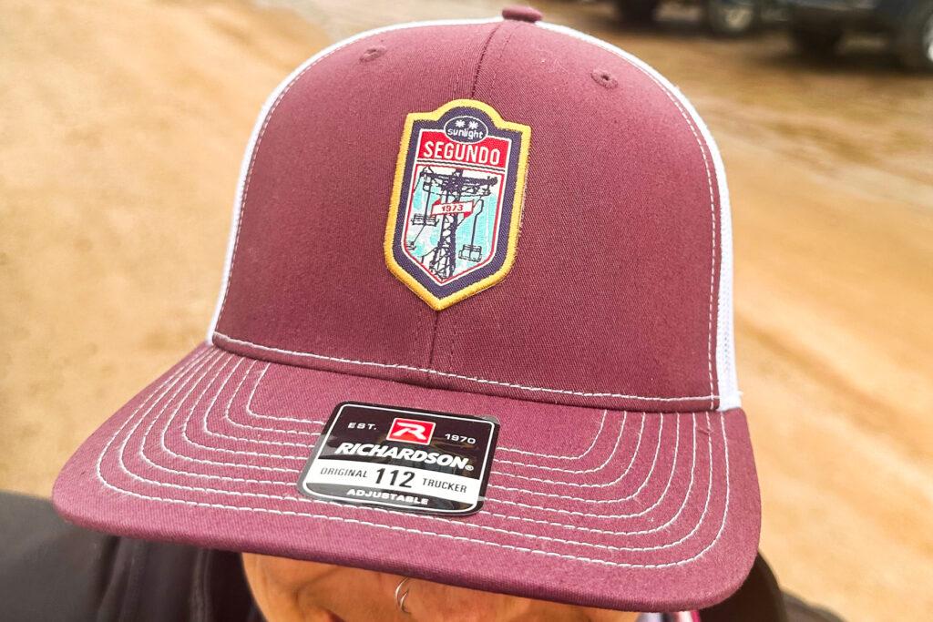 A woman wears a baseball cap showing with an image of a ski lift. It says Segundo started running in 1973.