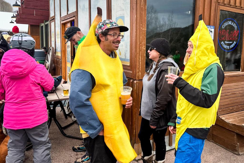 Two men dressed like bananas laugh and drink beers on a deck at Sunlight Ski Resort.