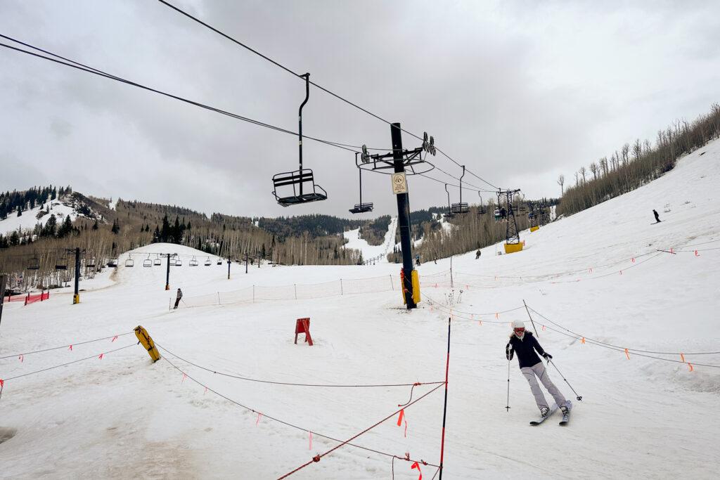 A ski lift slowly moves up a snowy mountain as people skier below it.