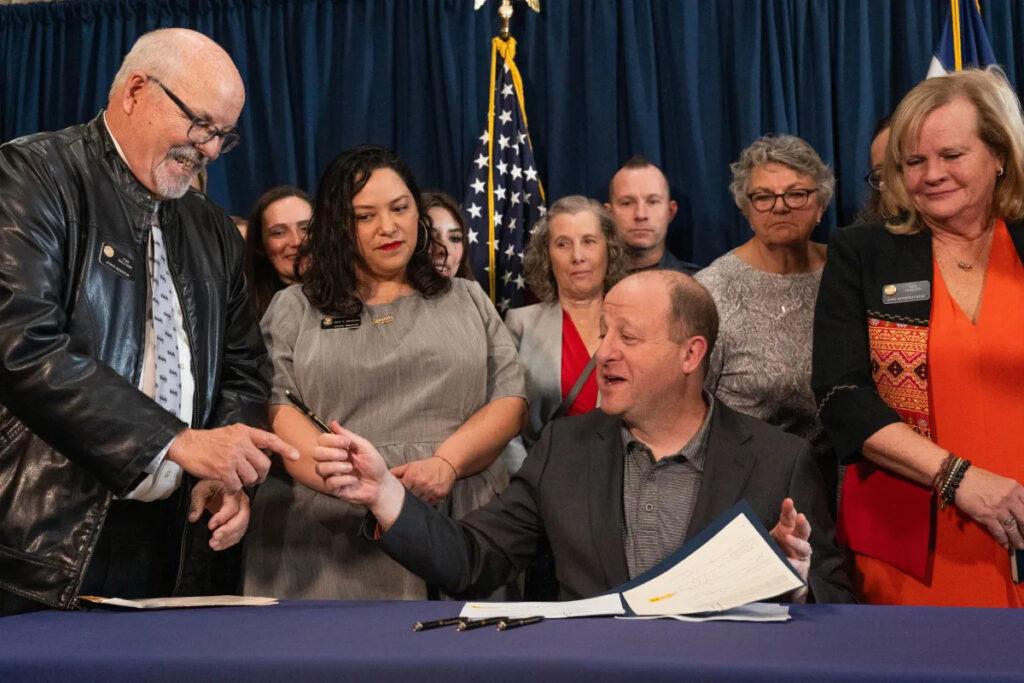 Colorado Gov. Jared Polis, center, hands a pen he used to sign Senate Bill 3 into law