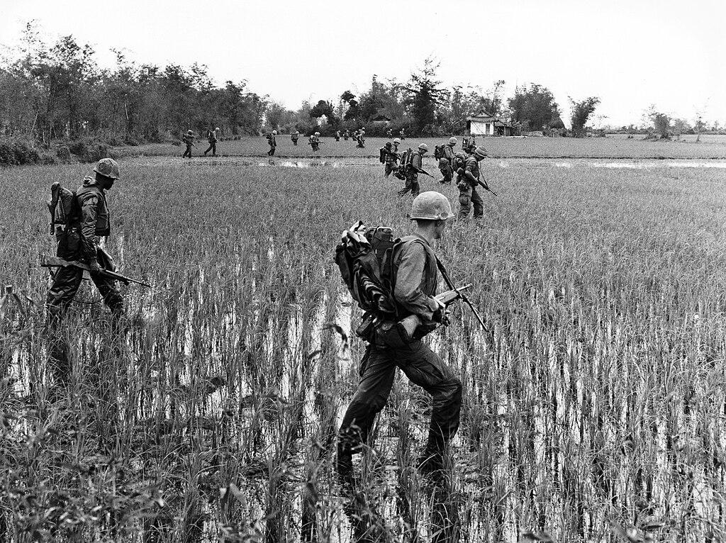 Troops with rucksacks and guns wade thorugh a paddy in Vietnam