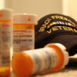 A baseball cap reading "IRAQUI FREEDOM VETERAN" on the counter next to multiple prescription pill bottles.
