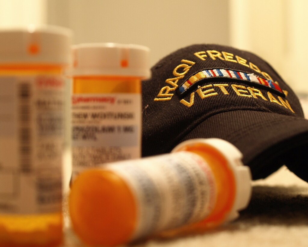 A baseball cap reading "IRAQUI FREEDOM VETERAN" on the counter next to multiple prescription pill bottles.