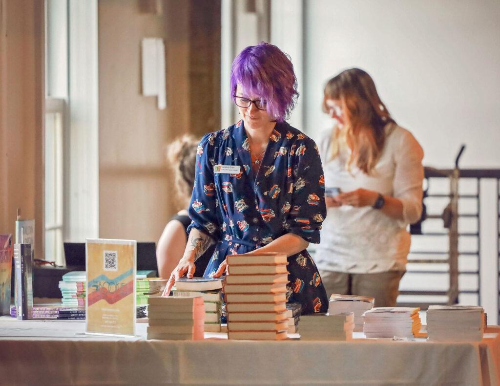 Valerie Eddy stands behind a table with stacks of books, arranging them.