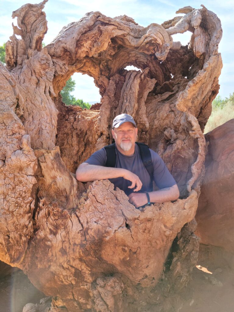 Man with grey goatee sits in petrified wood tree.