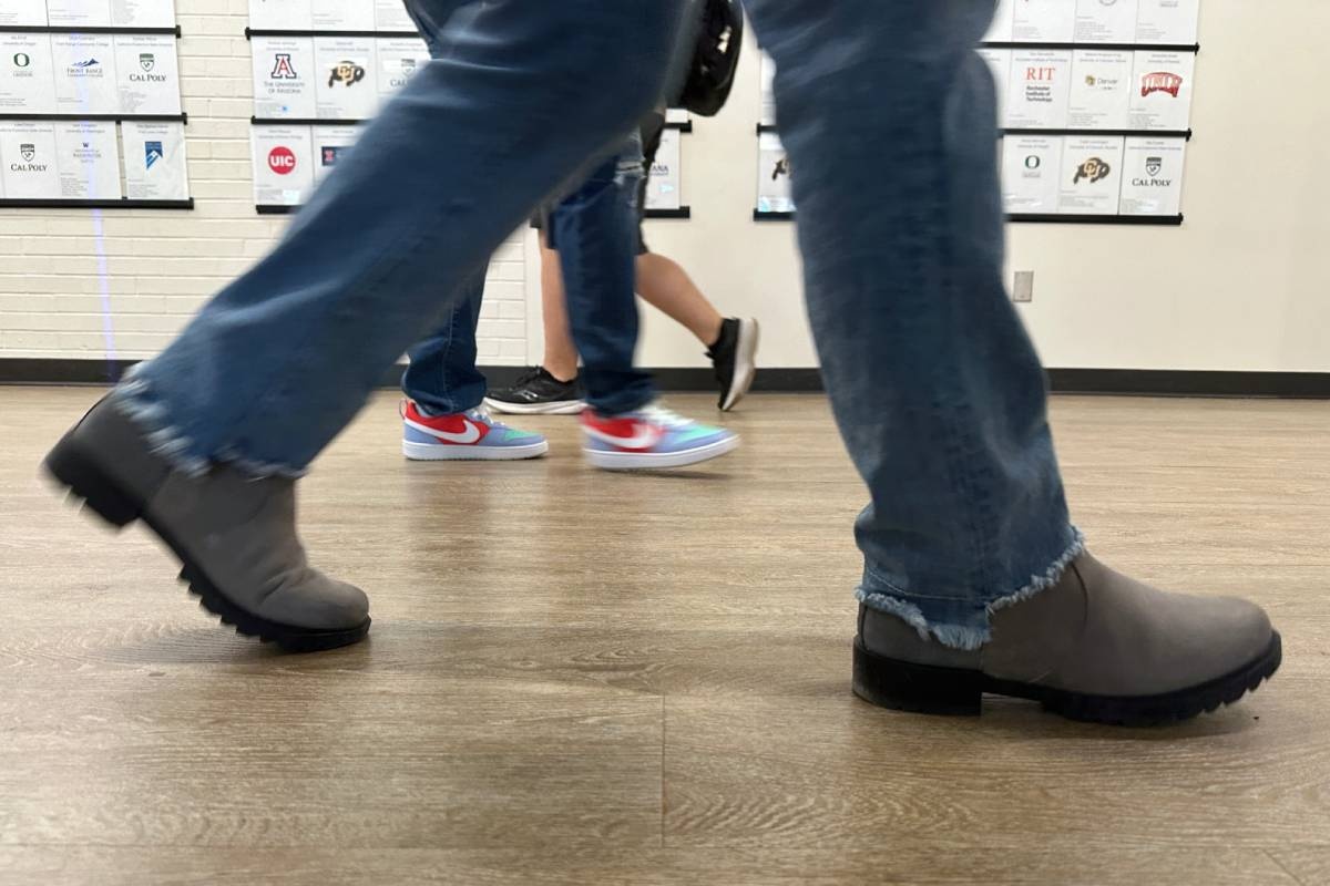 Three sets of students feet walking to class in a hallway.