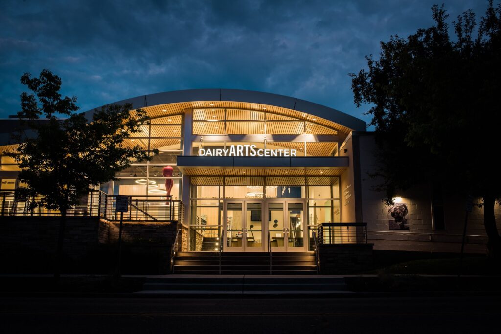 A building with a curved roof and floor-to-celing windows with a sign reading "DAIRY ARTS CENTER."