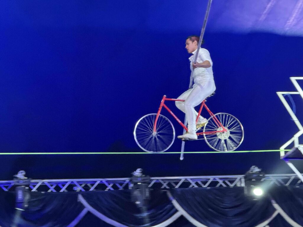 Man balancing long pole while riding bike on tight rope
