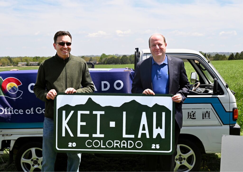Two men holding up a license plate sign KEI-LAW