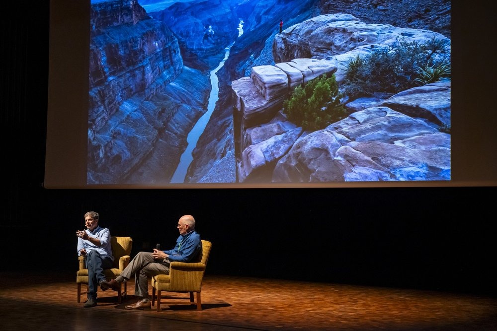 Hampton Sides and Kevin Fedarko sit in chairs on a stage with a projected scene of the Grand Canyon behind them.