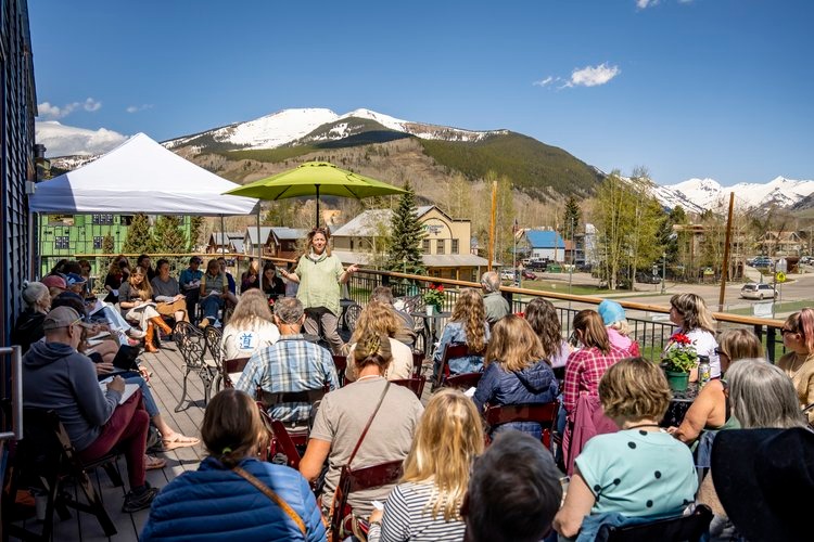 An audience sits on a patio with mountain views as presenter Pam Houston addresses the crowd.