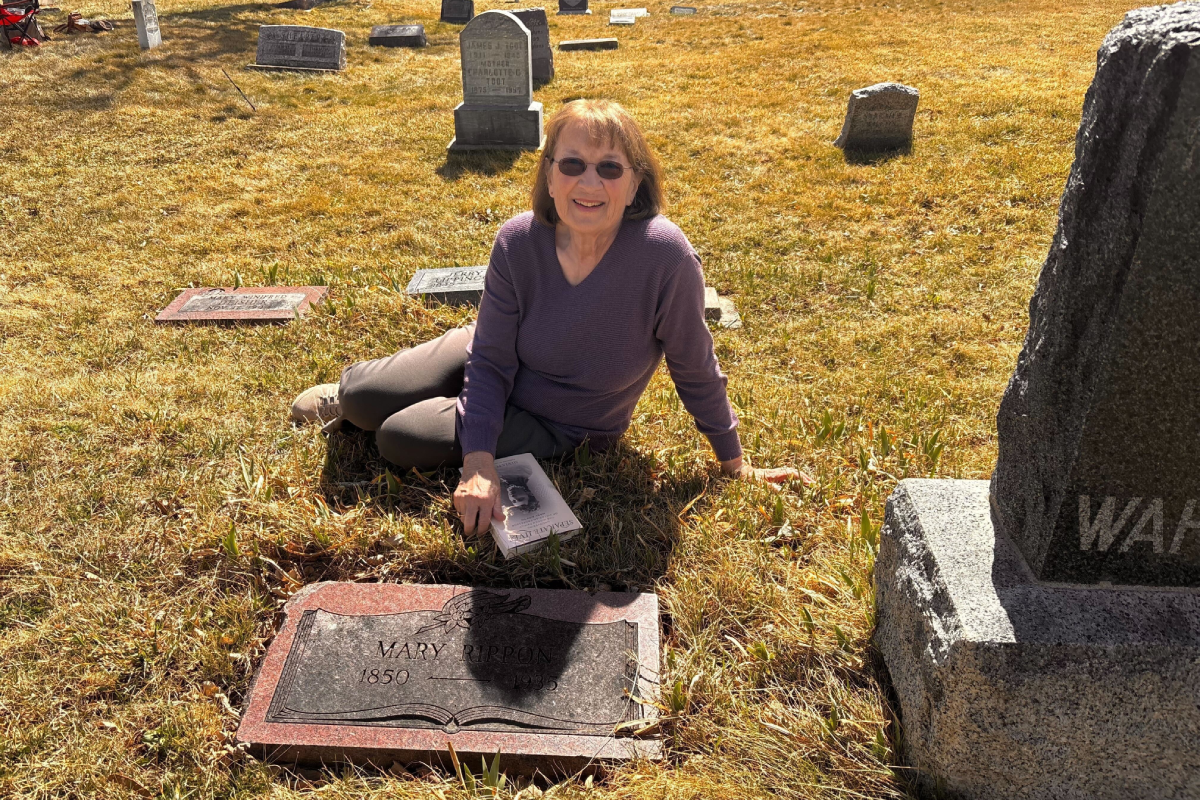 A woman is sitting on the ground next to a grave marker in a cemetery in Boulder.