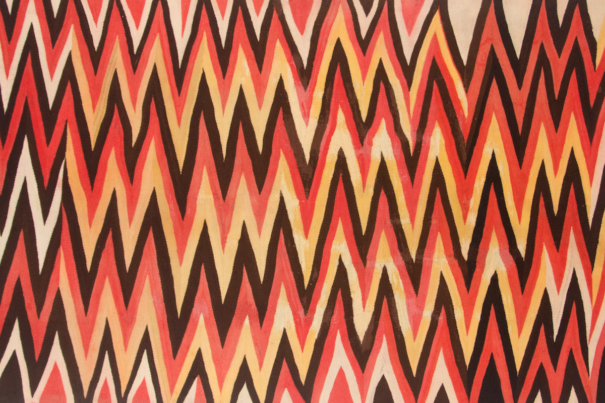 A close up of a flatweave rug with sharp zigzags in black, yellow, red and tan.