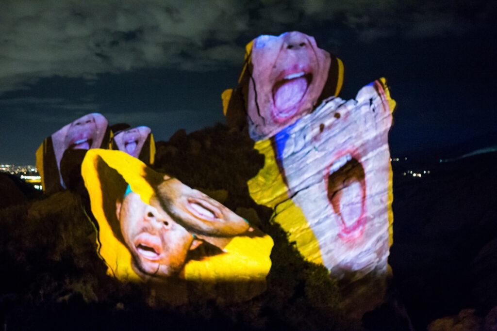 The lower halves of peoples faces projected on rocks in a field.